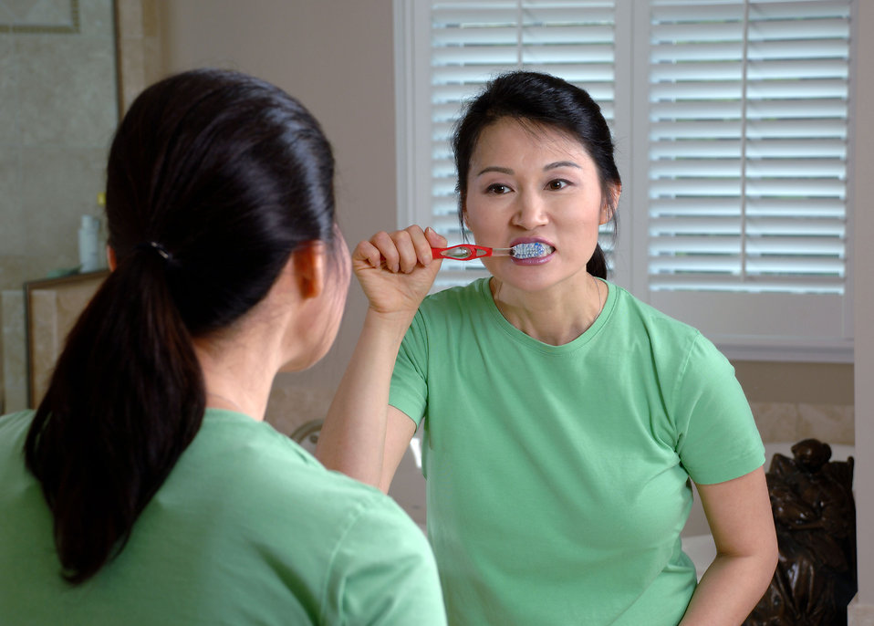 17067-an-asian-woman-brushing-her-teeth-in-a-mirror-pv
